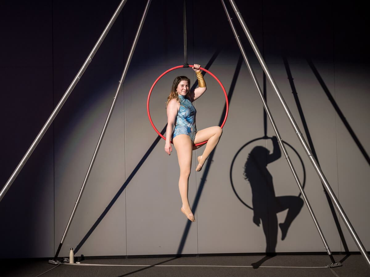 Aerial hoop performer suspended in a red hoop, casting a shadow on the wall behind